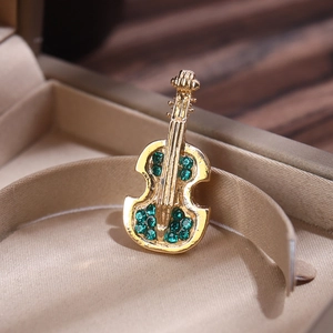 Macro view of gold violin brooch with green crystals on a beige jewelry case