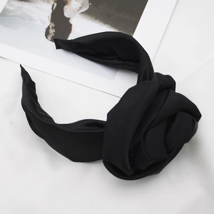 Detail of a black fabric headband with a large silk flower on a white background