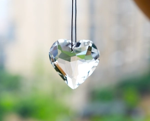 Macro shot of a heart-shaped crystal prism pendant hanging on a string with urban background