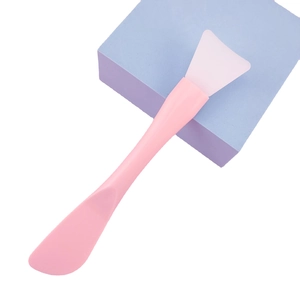 Pink silicone face mask brush with scraper tool for DIY beauty on purple geometric block
