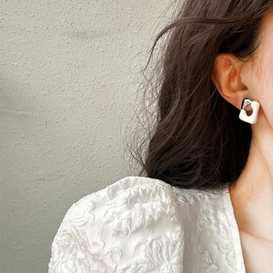 Close-up of geometric cream and silver stud earrings worn by a model in a minimal setting