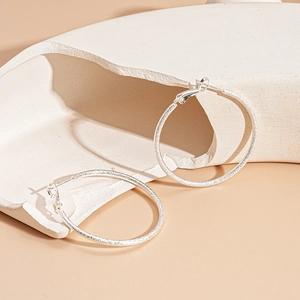 Close-up of silver hoop earrings with a matte textured finish on a stone platform