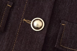 Détail de veste en jean avec surpiqûres dorées contrastées et bouton perle métallique