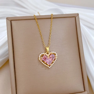 Elegant gold titanium necklace with hollow heart pendant and pink stones on a silk display