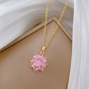 Macro detail of gold flower pendant featuring pink zircon stones on white silk background