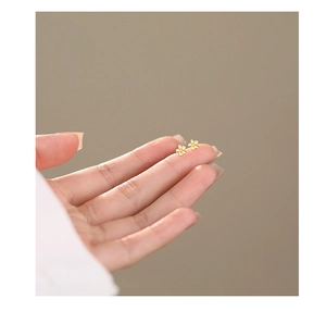 Macro shot of minimalist gold flower stud earrings held by hand for scale detail