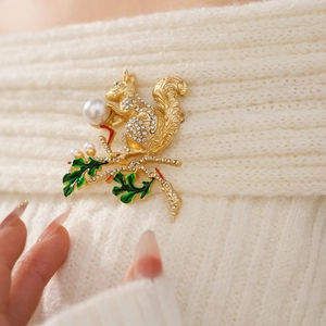 Vue détaillée d'une broche écureuil dorée avec strass et perle sur un pull en maille blanc