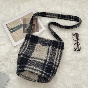 Overhead view of a plush black and white checkered shoulder bag on a soft white rug