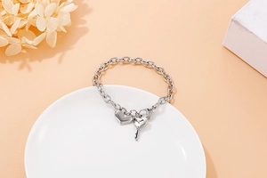 Close-up of silver heart and key charms on a polished stainless steel chain bracelet