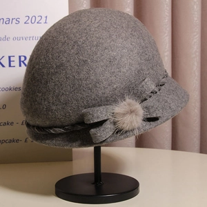 Detail of grey wool cloche hat featuring a plush fur ball and bow on a metal stand