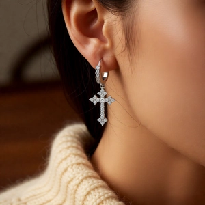 Close-up of sparkling zircon cross charm hoop earring worn on an ear with silver finish
