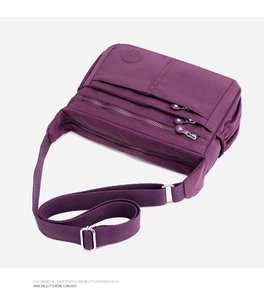 Vista detallada del bolso bandolera de nailon morado con cremalleras y correa ancha