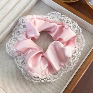 Pink satin scrunchie with white lace edges on wooden jewelry tray, elegant hair accessory