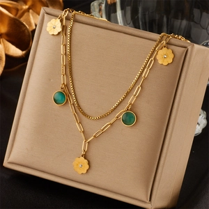 Macro detail of gold layered necklace with flower pendants and green gems on gift box