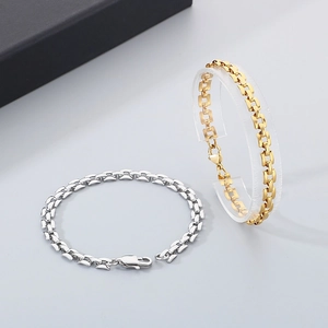 Detailed view of flat chain bracelets in gold and silver finishes on a neutral grey background