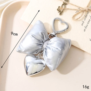 Silver bow heart keychain with metallic pendant and strap on a beige aesthetic background