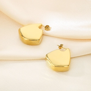 Détail macro de boucles d'oreilles plaquées or 18K sur un élégant tissu en soie champagne