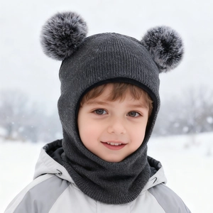 Detail of dark grey knit baby balaclava with dual fur pom-poms on snowy background