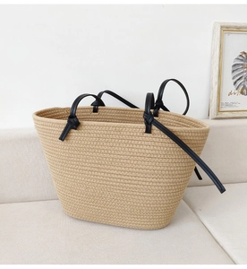 Detail of beige woven cotton rope tote with black leather knotted handles on a sofa
