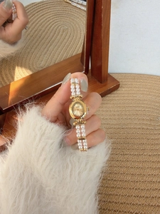 Detail of a vintage oval gold watch with double-layer pearl strap and mother of pearl dial