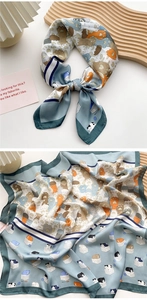 Detail of silk satin scarf featuring cute cartoon cats and paw prints on blue-grey fabric