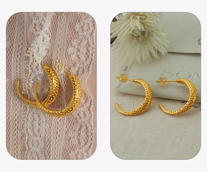Macro detail of gold C-shaped earrings with textured surface on white lace and floral decor