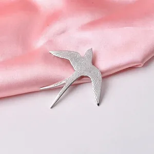 Dettaglio della spilla a rondine argento con piume incise su sfondo di raso rosa