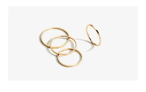 Macro detail of four minimalist 18k gold plated titanium steel rings on light background