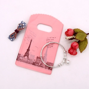 Silver metal bracelet with hollow ball and bell pendants on a pink decorative card