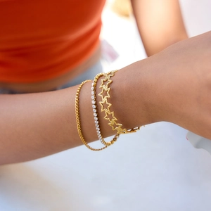 Makro-Detail von geschichteten Goldarmbändern mit Stern-Ausschnitt und Tennis-Kette am Handgelenk