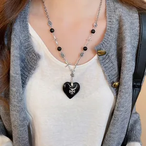 Gothic leather heart necklace with a silver cross pendant worn over a grey cardigan