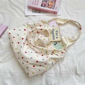 Vue détaillée d'un sac fourre-tout en toile crème à pois colorés contenant des livres