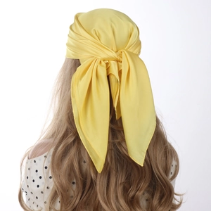 Detail view of bright yellow satin square scarf tied on hair with soft draped texture