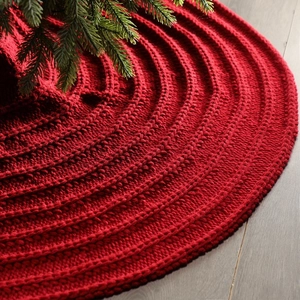 Red knit Christmas tree skirt with ribbed concentric patterns on grey wood floor