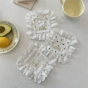 Detail of lace-edged cotton coasters with embroidered hearts on a marble table