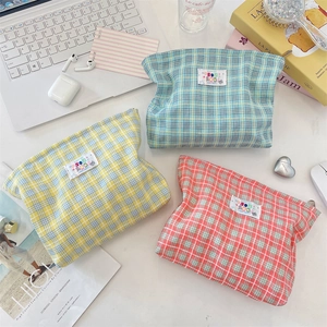 Tre pochette per cosmetici in tela a quadretti colorati disposte su una scrivania