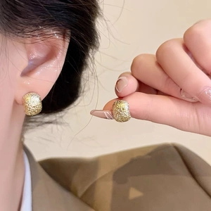Macro shot of minimalist gold frosted textured earrings showing refined metallic detail