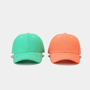 Mint green and orange cotton baseball caps with contrast stitching on gray background