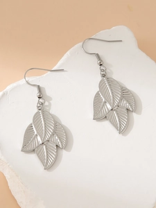 Detailed view of silver leaf-shaped stainless steel drop earrings on a textured block