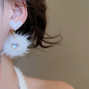 Detail of model wearing plush ball earrings with resin bear pendant and sparkling heart stone