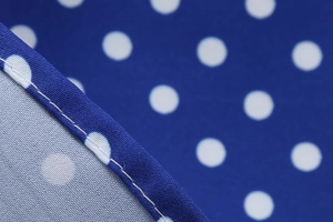Detailed close-up of blue polka dot fabric with white spots and neat edge stitching
