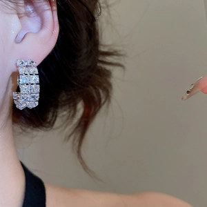 Close-up of C-shaped silver earrings with double rows of square cubic zirconia inlay