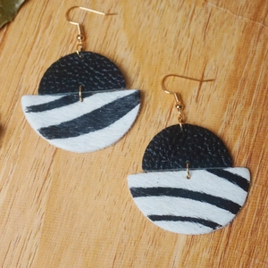 Détails des boucles d'oreilles en cuir imprimé vache sur un fond en bois naturel