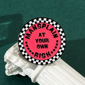 Close-up of a pink enamel pin with checkerboard border and a humorous slogan design