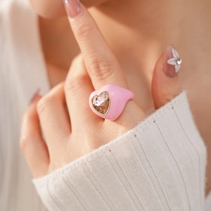 Detail of a pink enamel heart ring featuring a champagne gemstone on a model's hand