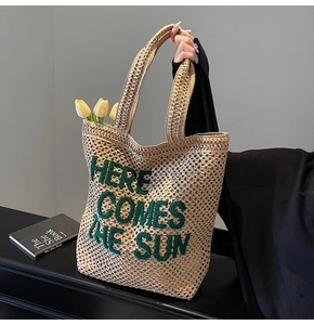 Detail of beige straw tote bag with green embroidered Here Comes The Sun text