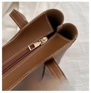 Détail d'un sac cabas marron avec surpiqûres blanches et fermeture éclair en métal doré