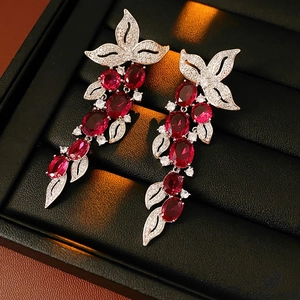 Détail de boucles d'oreilles à pompons en argent et pierres rouges dans une boîte noire