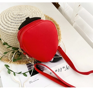Detail of red strawberry crossbody bag with gold chain and leaf decor on white desk