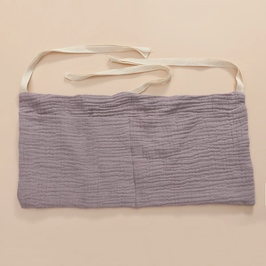 Detail of purple cotton storage bag with two pockets and white ties on soft beige backdrop